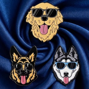 May include: Three enamel pins featuring dog breeds wearing sunglasses. The breeds include a golden retriever, a German shepherd, and a husky. Each pin has a different color scheme and tongue sticking out.