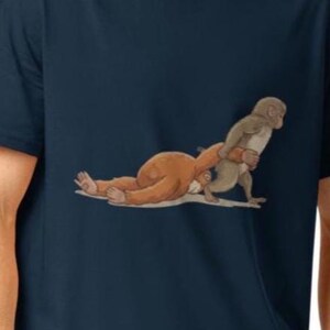 Könnte beinhalten: Marineblaues T-Shirt mit einer Cartoon-Illustration von zwei Affen. Ein Affe liegt, während der andere steht und den anderen zu tragen scheint. Die Affen sind braun und hellbraun.