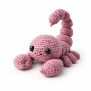 Peut inclure: Un scorpion crocheté à la main, de couleur rose poudré. Le scorpion a un corps arrondi, de grandes pinces et une queue incurvée. Il présente des yeux de sécurité noirs et est réalisé avec un point texturé.
