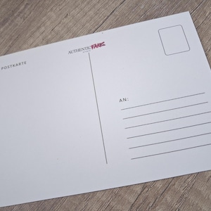May include: A white postcard with the text "POSTKARTE" and "AUTHENTIC PARIS" in the upper left corner. The postcard has a rectangular area for a stamp and lines for the recipient's address.