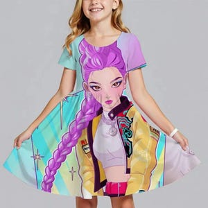 May include: A light blue, purple, and yellow dress featuring a cartoon illustration of a woman with purple hair and a yellow jacket. The dress has short sleeves and a flared skirt. The illustration is centered on the front of the dress.