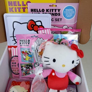 Pode incluir: Um conjunto de presentes Hello Kitty numa caixa de cartão. O conjunto inclui um brinquedo de pelúcia, livros para colorir, lápis, autocolantes, uma bandeja de metal e outros acessórios. Os itens são principalmente rosa, branco e vermelho, com o logotipo Hello Kitty.