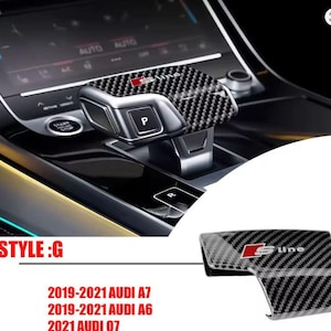 Op de afbeelding: Carbon fiber versnellingspook cover voor Audi voertuigen. De cover heeft een zwart en grijs geweven patroon met het "S line" logo in rood. De afbeelding toont ook de versnellingspook en de tekst "STYLE: G". Compatibel met Audi A7, A6 en Q7 modellen.