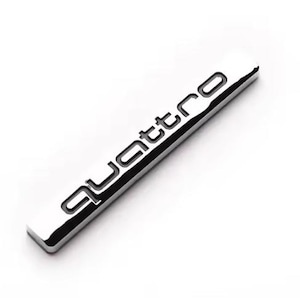 May include: A rectangular, chrome emblem with the word "quattro" in black lettering. The emblem is angled, displaying its reflective surface. The design is sleek and modern, set against a white background. The emblem is likely for a vehicle.