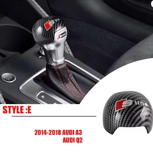Pode incluir: Manípulo da alavanca de câmbio em estilo fibra de carbono com costuras vermelhas na bota de couro. O manípulo tem o logótipo S line e foi concebido para os modelos Audi A3 e Q2. Um manípulo sobresselente também é mostrado.