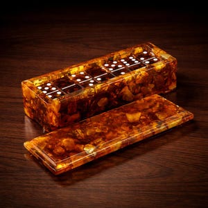 May include: A rectangular domino set with a matching lid. The set is encased in a translucent amber-colored material, revealing the embedded stones. The dominoes have white dots. The lid is placed next to the set on a dark wooden surface.