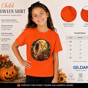 Puede incluir: Una camiseta naranja de manga corta con un gráfico circular de un ángel en un campo de calabazas con girasoles y una luna llena. La prenda es 100% algodón, lavable a máquina y está disponible en tallas juveniles de la XS a la XL.