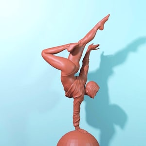 Peut inclure: Une sculpture de couleur terre cuite représentant une personne en équilibre sur une main, l'autre bras et jambe tendus. La figurine est posée sur une base sphérique. Le fond est bleu clair uni.