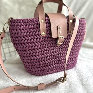 Peut inclure: Sac fourre-tout en crochet violet fait à la main, avec rabat et poignées en cuir. Le sac est doté d'une bandoulière amovible rose clair et d'une quincaillerie dorée. La texture tissée et la couleur du sac en font un accessoire élégant.