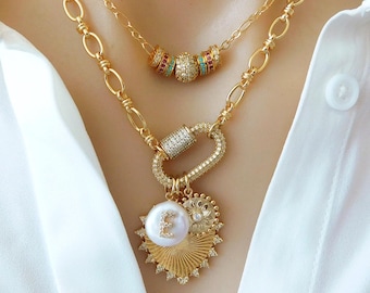 May include: Gold-toned necklaces with multiple layers. The top layer features a chain with colorful beaded accents. The second layer has a large clasp with a pearl pendant, a sunburst charm, and a charm with the letter "E".