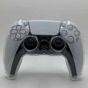 May include: A transparent protective cover for a white and black games controller. The controller features a white central panel, black detailing, and clear buttons. The cover is clear, allowing the controller's design to be seen.