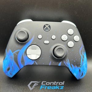 May include: An Xbox controller with a black finish and a blue flame pattern. It has grey thumbsticks, buttons, and a white D-pad. The Control Freakz logo is displayed at the bottom of the controller.