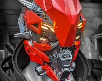 Op de afbeelding: Een rood en zwart robothelm met een geometrisch ontwerp en verlichte gele lichtaccenten. De helm toont de tekst TWOHORNSUNITED en BRIAN TWOHORNS DESIGNS in de rechterbovenhoek, met ingewikkelde mechanische details.