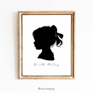 Peut inclure: Une impression d'art encadrée avec une silhouette noire d'une jeune fille avec un nœud dans les cheveux. L'impression comprend le nom "Faith McCoy" en cursive et le logo Willowbrook Made Co. Le cadre est de couleur marron clair.