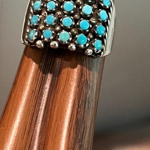 May include: A silver ring featuring a rectangular cluster of numerous small, round, bright blue turquoise stones set in individual bezels. The band is constructed with a twisted silver wire border along the sides, framing the turquoise inlay.
