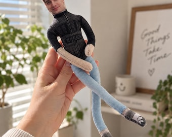 Könnte beinhalten: Eine personalisierte Stoffpuppe mit einem aufgedruckten Foto eines Gesichts auf dem Kopf. Die Puppe trägt eine schwarze langärmelige Jacke mit Reißverschluss, eine hellblaue Hose im Jeans-Stil und dunkelgraue Schuhe mit weißen Schnürsenkeln.