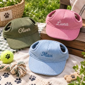 May include: Three corduroy pet hats in olive green, pink, and light blue. Each hat features ear holes and white embroidered names: Oliver on the green hat, Luna on the pink hat, and Max on the blue hat. The hats have a structured brim design.