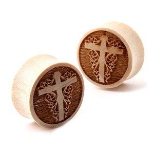 May include: A pair of wooden ear gauges with a cross design. The cross is carved into the wood and has a floral pattern around it.