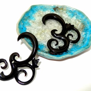 May include: Two black wooden ear gauges with a spiral design. The gauges are on a blue and white background.