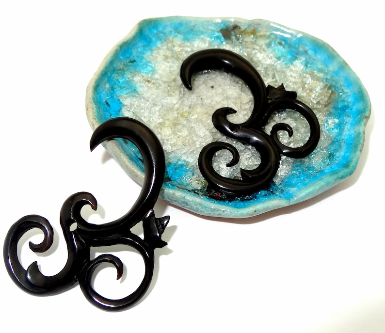 May include: Two black wooden ear gauges with a spiral design. The gauges are on a blue and white background.