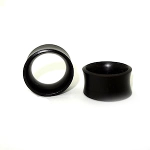 May include: Two black wooden ear gauges, one is a simple ring shape and the other is a flared shape.