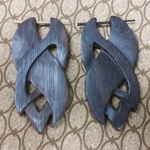 May include: A pair of dark brown wooden earrings with intricate knot designs. The earrings are made of a dark wood with a natural grain pattern. Each earring has a small hole at the top for a hook or post.