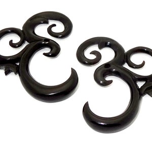 May include: A pair of black horn ear gauges with a swirling, ornate design. The gauges are made of natural horn and have a smooth, polished finish.