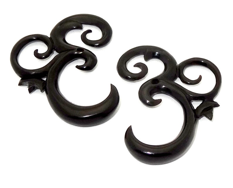 May include: A pair of black horn ear gauges with a swirling, ornate design. The gauges are made of natural horn and have a smooth, polished finish.
