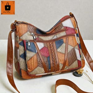 Puede incluir: Bolso bandolera patchwork multicolor con correas de cuero marrón. El bolso presenta una variedad de formas geométricas en tonos naranja, azul, rojo y blanco. Tiene múltiples compartimentos con cremallera y un detalle trenzado en el centro.