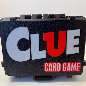 May include: Black rectangular Clue card game box with white and red lettering. The word "CLUE" is prominently displayed, with "CARD GAME" below. The box has a textured surface and a clasp closure.