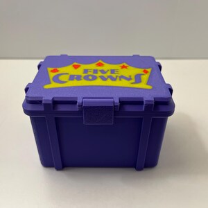 May include: A small, purple box with a hinged lid. The lid displays the words "FIVE CROWNS" in yellow, with a crown and star design. The box is made of a durable material and has a secure latch.