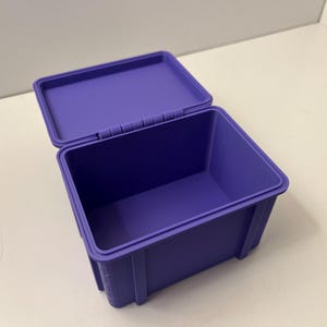 May include: A purple plastic storage box with a hinged lid, open to reveal the interior. The box is rectangular with a smooth finish. The lid is slightly ajar, showing the inside of the box.