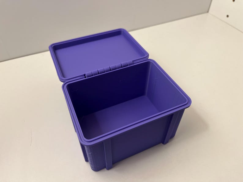 May include: A purple plastic storage box with a hinged lid, open to reveal the interior. The box is rectangular with a smooth finish. The lid is slightly ajar, showing the inside of the box.
