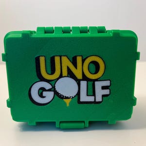 May include: A green plastic case with the words "UNO GOLF" printed on the front. The design includes a golf ball and tee. The case has a textured surface and a hinged lid with a clasp.