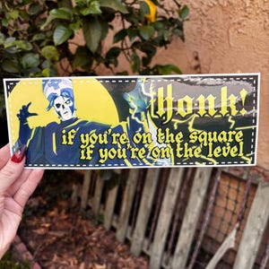 May include: A rectangular bumper sticker featuring a character in blue and white attire against a yellow backdrop. The text reads "Honk! if you're on the square if you're on the level."