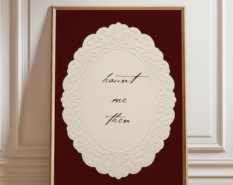 May include: Framed art print featuring the words "haunt me then" in elegant script within a cream-colored, ornate oval design. The background is a deep burgundy, and the frame is a warm brown.