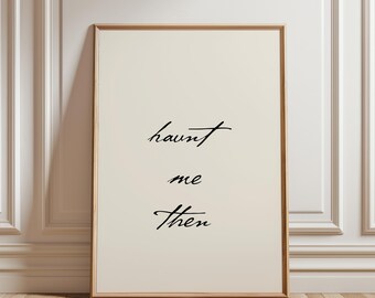 May include: A rectangular framed wall art piece featuring a light cream background with the black cursive text "haunt me Then" centered in the middle. The frame is made of light-colored wood and has a simple, clean profile surrounding the print.