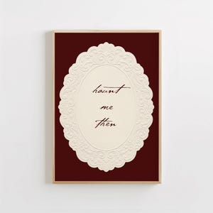 May include: A rectangular wall art print featuring a deep burgundy background and a central cream-colored oval frame with an embossed floral border. The text "haunt me then" is written in the center in a dark brown cursive script font.