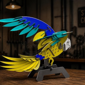 May include: A metal parrot sculpture with yellow, blue, and teal wings and tail feathers. The parrot is perched on a black stand. The sculpture has a detailed design and is made of steel. The background includes a sign that says "STEEL CRAFT".