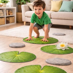 May include: A child plays on a set of green lily pad floor mats and gray stepping stones. A white water lily with a yellow center rests on one of the lily pads. The scene is set in a living room.