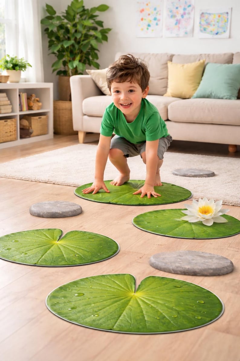 May include: A child plays on a set of green lily pad floor mats and gray stepping stones. A white water lily with a yellow center rests on one of the lily pads. The scene is set in a living room.