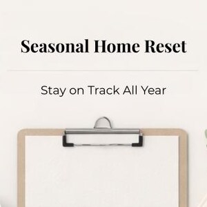 Könnte beinhalten: Ein Klemmbrett mit einem leeren weißen Papier, einer silbernen Klammer und einer hellbraunen Rückseite. Der Text "Seasonal Home Reset" und "Stay on Track All Year" sind über dem Klemmbrett zu sehen. Auf der rechten Seite ist eine kleine grüne Pflanze zu sehen.
