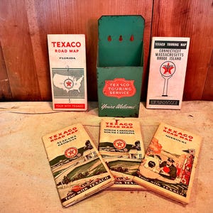 May include: Collection of vintage Texaco road maps and a green metal Texaco Touring Service holder. The maps feature state names like Florida, Connecticut, Massachusetts, Rhode Island, Alabama, Georgia, North Carolina, South Carolina, and Missouri.
