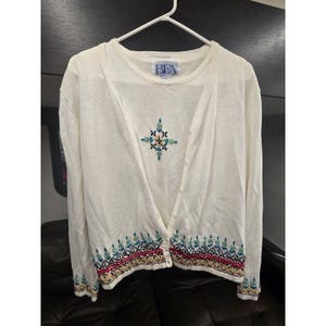 May include: Cream-colored cardigan and matching top. The cardigan has a button-up front and features an embroidered floral design in the center and along the bottom hem. The top has the letters "BFA" on the upper left side.