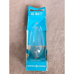 May include: A clear, teardrop-shaped light bulb in a blue and white cardboard box. The box is labelled "40 WATT" and "GENERAL ELECTRIC". The bulb is visible through a cutout in the box. The bulb is a 40-watt bulb.