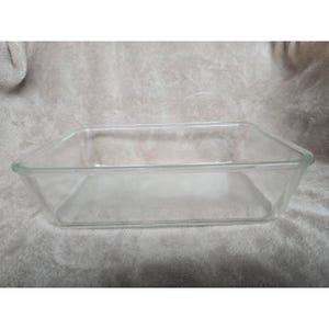 Puede incluir: Una fuente rectangular de vidrio transparente. El plato tiene un diseño sencillo con lados ligeramente ensanchados y esquinas redondeadas. Está vacío y parece sin usar.