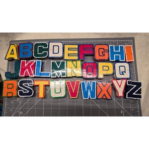 Peut inclure: Un ensemble complet de vingt-six blocs de puzzle alphabet en plastique, chacun en forme de lettre de A à Z dans diverses couleurs dont le rouge, le bleu, le vert, le jaune et l'orange. Les lettres sont disposées sur trois rangées.