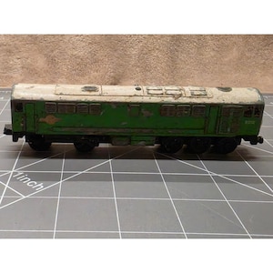 May include: A vintage toy train locomotive featuring a green body with a white roof and weathered paint. The side displays the number D5722 and a small circular emblem. The train is positioned on a cutting mat with a visible 1-inch measurement scale.