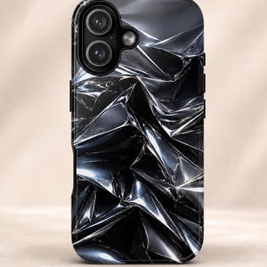 Könnte beinhalten: Eine rechteckige Handyhülle mit einem kontrastreichen, abstrakten Design, das das Aussehen von zerknitterter, reflektierender schwarzer und silberner Metallfolie nachahmt. Die Oberfläche zeigt scharfe, kantige Falten und tiefe Schatten.