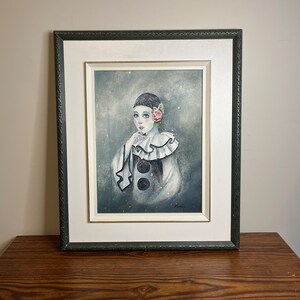 Könnte beinhalten: Gerahmtes Kunstwerk mit einem Aquarellgemälde einer Person in einem Pierrot-Kostüm. Die Figur hat helle Haut, dunkles Haar und eine rosa Rose. Das Gemälde befindet sich in einem grünen Rahmen.